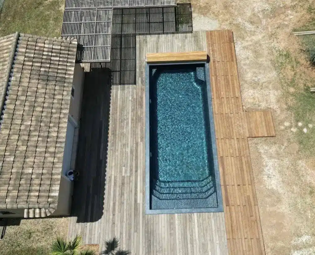 Piscine coque Freedom au revêtement sombre, vue du ciel, entourée d'une terrasse en bois